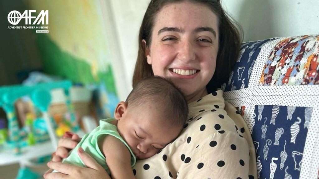 Missionária sorrindo com bebê rejeitado dormindo em seu colo.