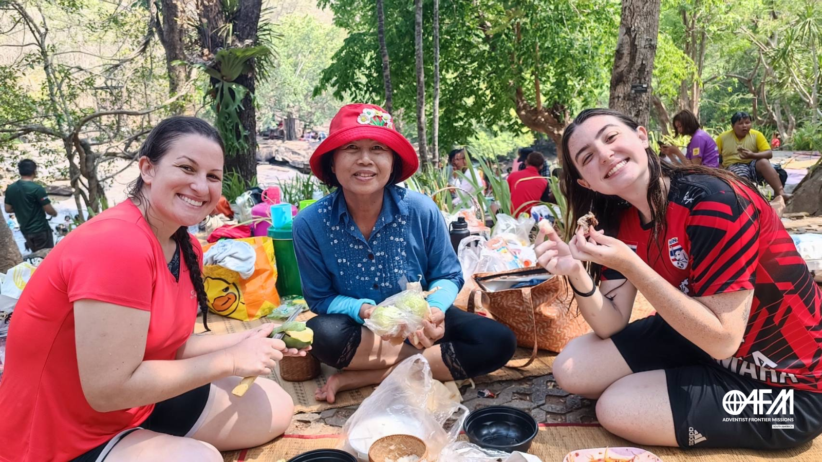 Um encontro inesperado, uma tailandesa e duas brasileiras comendo manga num piquenique em uma cachoeira na Tailândia.